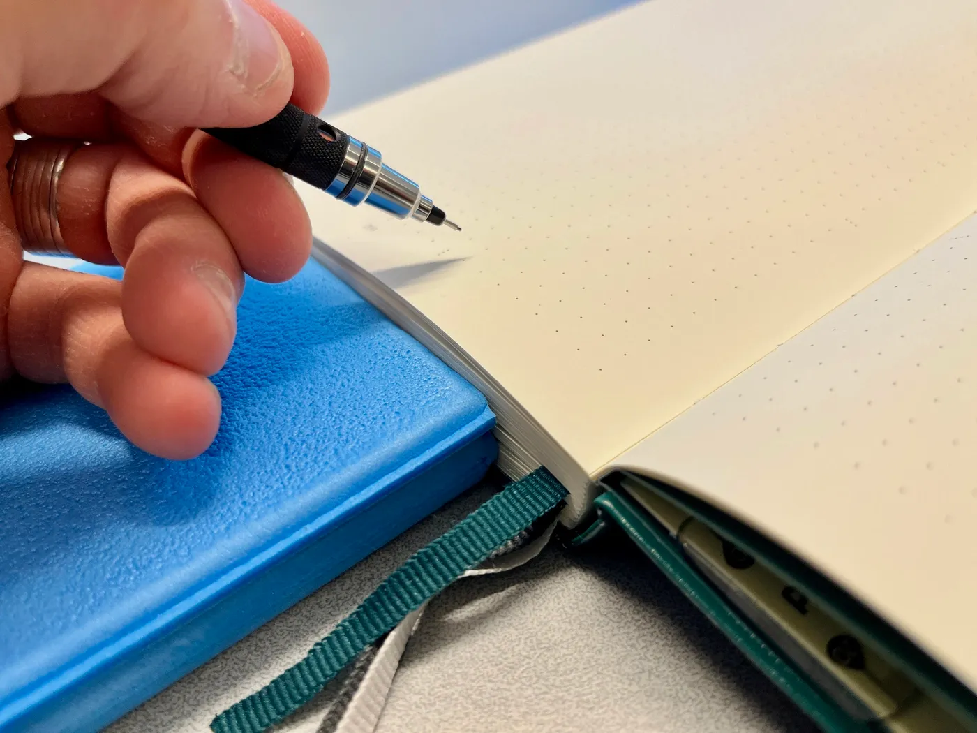 A picture of me holding a pen with the hand placed on the writing cushion on the thick edge of the notebook.