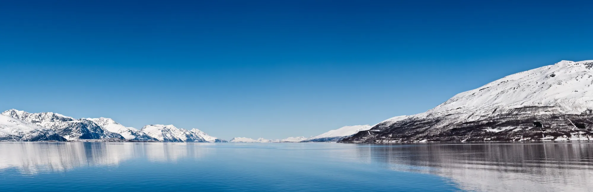 A quite blue picture of the Lyngen Fjord in Norway. Mountains and the blue sky reflecting in the water.