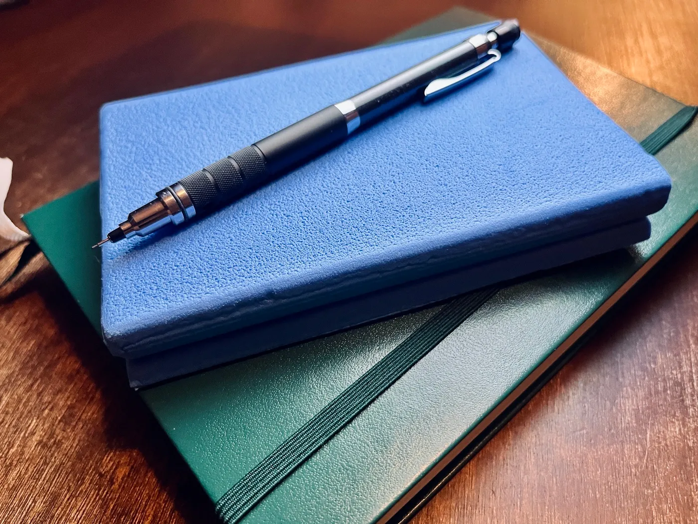 A picture of a A4 notebook with the writing cushion on top. On the latter is placed a Kuru Toga mechanical pencil 